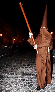 Penitent dressed in brown penitential robe (nazareno) carrying large candle at night, Semana Santa, Holy Week Procession, Huelva, Andalusia, Spain