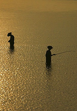 Silhouettes of fishermen standing in the water at sunset