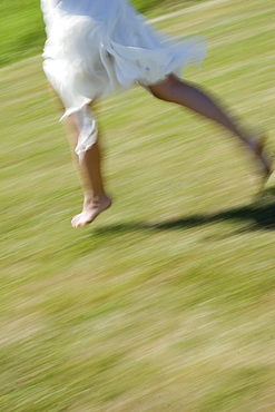 Young woman runs in a white dress without shoes over a meadow