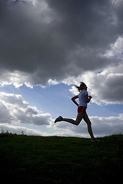 Running woman as a silhouette in front of a sky with dark clouds