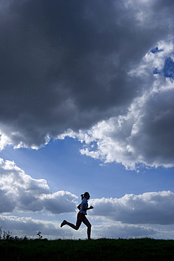 Running woman as a silhouette in front of a sky with dark clouds