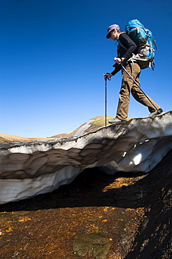 Female hiker walking on a snow slab, on the Laugavegur hiking trail, Hrafntinnusker-âˆšÃ…lftavatn, Fjallabak Nature Reserve, Highlands of Iceland, Iceland, Europe