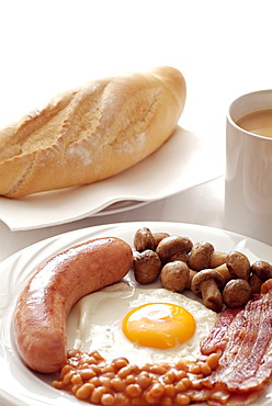 Traditional English Cooked Breakfast of Sausage, Egg, Bacon, Mushrooms and Beans. Served with a Mug of Tea.