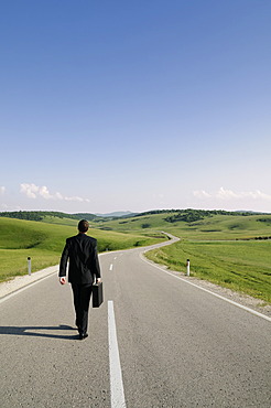 Businessman walking along a lonely country road, rear view