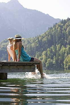 Young women sitting on a landing stage on Lake Schwansee near Fuessen, Allgaeu region, Bavaria, Germany, Europe