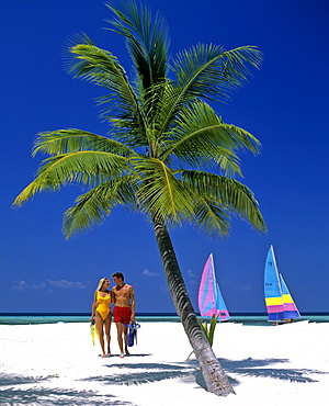 Palm tree, young couple on the beach with snorkeling gear, catamarans, Maldives, Indian Ocean