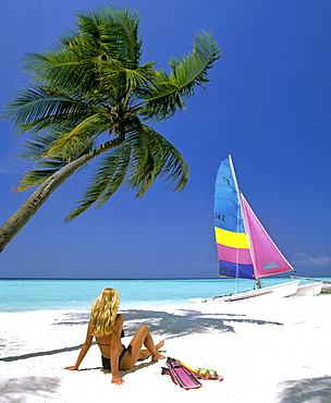 Young woman with snorkeling gear on sandy beach, catamaran and palm tree, Maldives, Indian Ocean