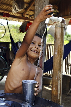 Boy filling water into a drinking vessel, Amazon Basin, Brazil