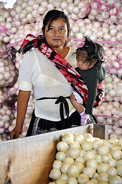 Indigene woman carrying a small girl in a sling, standing in front of bags of onions, CENMA, vegetable wholesale market in the south of Guatemala City, Guatemala, Central America