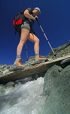 Hiker crossing a wooden bridge above a mountain brook, National Park Hohe Tauern, Tyrol, Austria