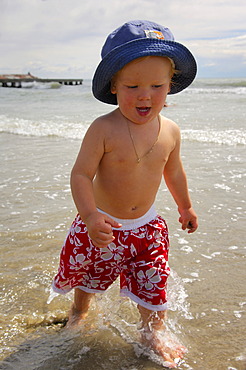 Little boy on the beach running through the water, Caorle, Veneto, Italy