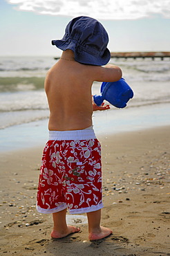 Little boy on the beach playing with a watering can, Caorle, Veneto, Italy