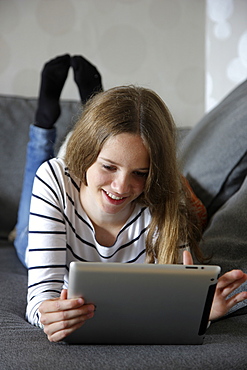 Girl lying on a sofa holding an iPad, tablet computer with wireless internet access