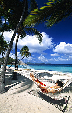 Woman in a hammock under palm trees on a beach on Peter Island, British Virgin Islands, Caribbean