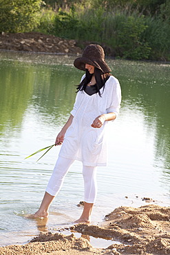 Young woman wearing a straw hat on the beach of a quarry pond