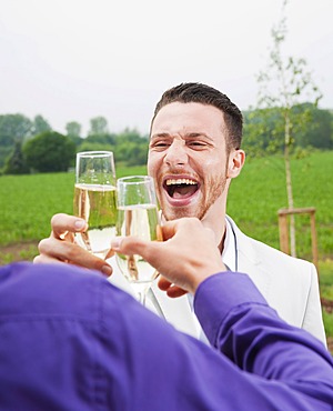 Happy young man, chinking glasses, celebrating on a terrace