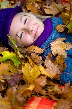 Girl, 13, lying between colourful autumn leaves