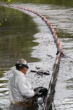 A worker vacuums oil from behind a containment boom on the Kalamazoo River during the cleanup of a major oil spil in which 800, 000 gallons of oil spilled from an Enbridge Energy Partners pipeline, Battle Creek, Michigan, USA