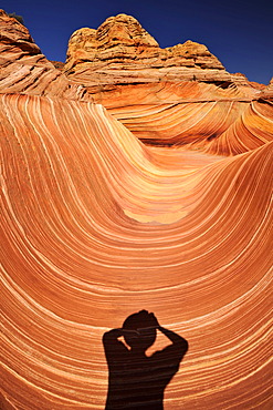 Shadow of a photographer on The Wave, banded eroded Navajo sandstone rocks with Liesegang Bands, Liesegangen Rings, or Liesegang Rings, North Coyote Buttes, Paria Canyon, Vermillion Cliffs National Monument, Arizona, Utah, USA