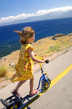 Child riding on its scooter at the coast, Peloponnese, Greece