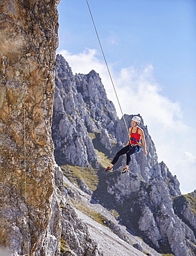 Climber with helmet swinging on climbing rope on rock face, Northern Alps, near Innsbruck, Tyrol, Austria, Europe