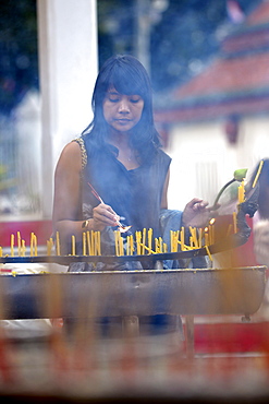 Woman lighting candles outside the Wat Phra Si Rattana Mahathat Temple, Phitsanulok, Northern Thailand, Thailand, Asia