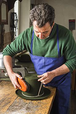 Man brushing a dry wool felt hat, holding shaping cord in his hand, hatmaker workshop, Bad Aussee, Styria, Austria, Europe