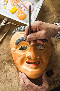 Painting the face of a wooden mask with a paintbrush, on a workbench, wooden mask carver, Bad Aussee, Styria, Austria, Europe