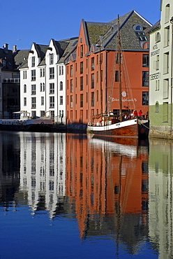 Houses and a sailing boat reflected in the calm water of the inner harbor of Alesund, Alesund, Moere og Romsdal, Norway, Europe