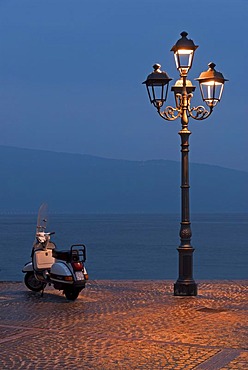 A Motorino scooter beside a street lamp at the shore of Lake Garda at the blue hour in Gargnano, Lombardia, Italy, Europe