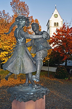 Statue of a dancing couple on a well, surrounded by 23 columns with heads made of bronze, in front of the Catholic Mariae Himmelfahrt Church, Immenstaad, Baden-Wuerttemberg, Germany, Europe