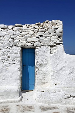 Small narrow blue wooden door in a whitewashed wall of rough stones, Mykonos, Greece, Europe