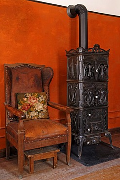 Fauteuil chair and cast-iron stove, 1900, living room in the teacher's apartment, school building from Pfaffenhofen, built in 1801, Franconian open-air museum, Eisweiherweg 1, Bad Windsheim, Middle Franconia, Bavaria, Germany, Europe