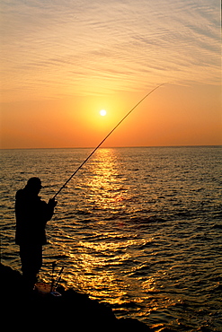 Silhouette of fisherman casting fishing line into sea at sunset