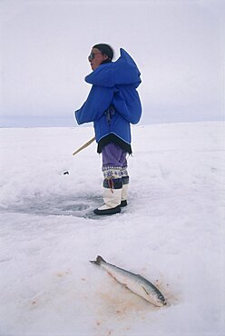 Image of an Eskimo woman ice fishing on a frozen lake in Baffin Canada