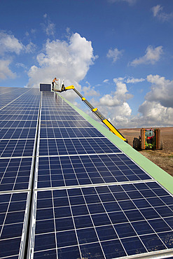 Photovoltaic panels installed on the roof of a farm building against a blue sky with light clouds, France