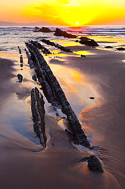 parallel rock formations on sea shore in tidal zone of sea with sun at sunset sunrise in background contre-jour shot backlit outdoors La Rasa Mareal flysch cliffs Basque Country Spain Europe