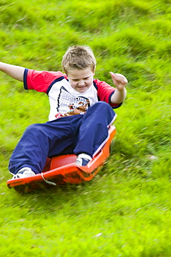 A young boy sledging down a grassy bank