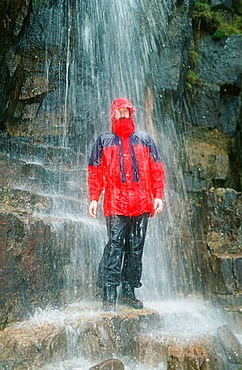 A man testing a waterproof jacket under a waterfall in Scotland, United Kingdom, Europe