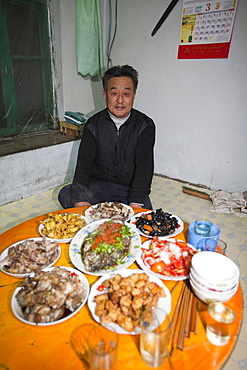 A Chinese man sitting cross legged for a traditional meal in Heilongjiang Province, Northern China, Asia