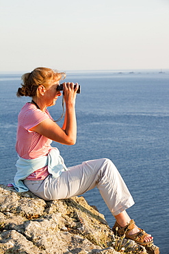 A woman birdwatching off sea cliffs on Cape Cornwall in Cornwall, England, United Kingdom, Europe