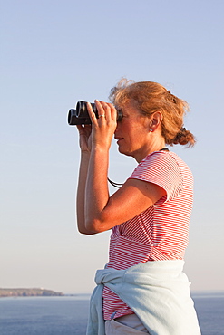 A woman birdwatching off sea cliffs on Cape Cornwall in Cornwall, England, United Kingdom, Europe