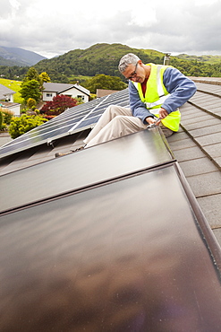 A workman fitting solar thermal panels for heating water, to a house roof in Ambleside, Cumbria, England, United Kingdom, Europe