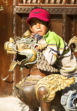 A young boy sitting on a copper sculpture at a religious site in Kathmandu, Nepal, Asia