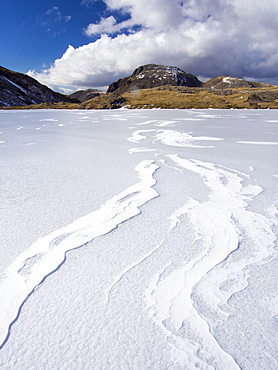 Wind drifted snow on Sprinkling Tarn at the head of  Borrowdale, frozen solid, looking towards Great End, Lake District, Cumbria, England, United Kingdom, Europe