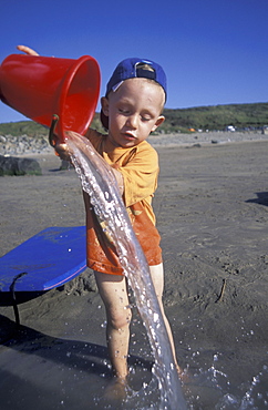 Boy pouring water from a bucket, Whitesands Beach, St Davids, Pembrokeshire, Wales, UK, Europe