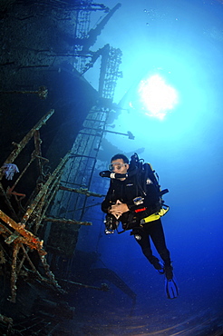 Mixed gas rebreather divers by ship wreck, sunburst on surface behind.  Red Sea.