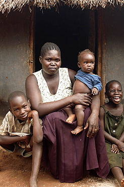 Typical of housing in Gulu Town, the simple mud hut accommodates many of it's residents.  Here a family are posing for a picure in fromt of theirs.  The father is missing, who is out at work.  Gulu, Uganda. Gulu Town, Uganda, East Africa