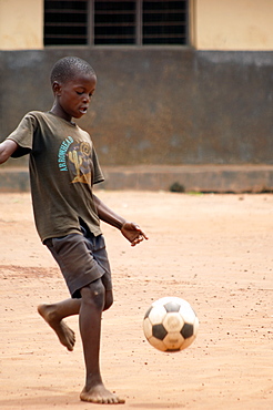 Young African boy playing football in the school yard.  Guly Town, northern Uganda. Gulu Town, Uganda, East Africa