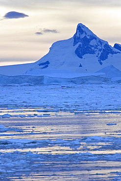 Sunset on snow capped mountains and icebergs surrounded in brash ice in Crystal Sound near the Antarctic Circle on the west side of the Antarctic Peninsula.